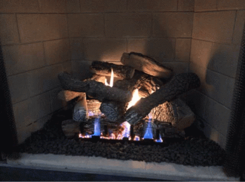 A Fireplace Filled With Logs And A Blue Flame GIF