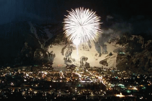 A Fireworks Display In Front Of A Snowy Mountain Over A City GIF