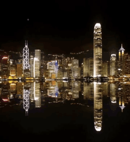 A Fireworks Display Over A City With A Reflection In The Water GIF