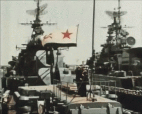 A Flag With A Red Star On It Is Flying In Front Of A Military Ship GIF