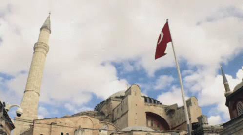 A Flag With The Letter C On It Is Flying In Front Of A Large Building GIF