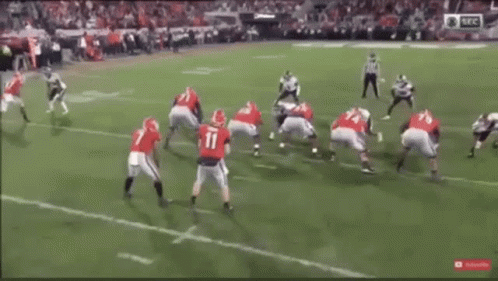 A Football Game Is Being Played On A Field With A Referee In The Background . GIF