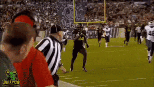 A Football Game Is Being Played On A Field With A Referee Standing In The Middle . GIF