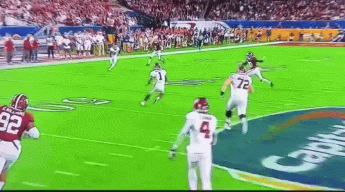 A Football Game Is Being Played On A Green Field With A Crowd In The Background . GIF