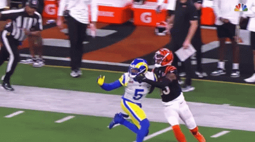 a football player in a blue and yellow uniform is trying to catch a pass from another player in a black uniform .