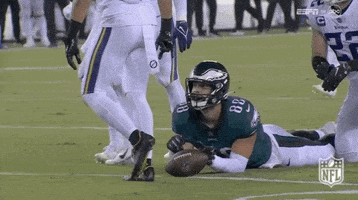 a football player in a green uniform is laying on the field with a ball .