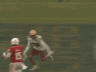 a football player in a red jersey and white pants is being tackled by another player on the field .
