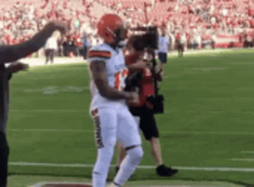a football player is dancing on the field while a cameraman takes a picture .