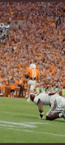 A Football Player Is Kneeling On The Field In Front Of A Crowd While Another Player Runs With The Ball . GIF