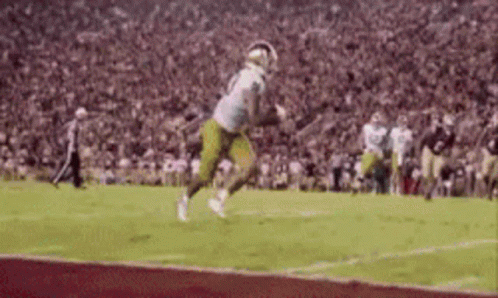 A Football Player Is Running On A Field With A Ball In His Hand . GIF