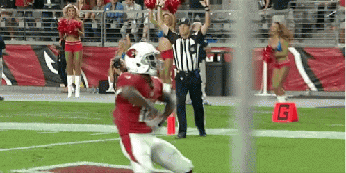 A Football Player Is Running On The Field With Cheerleaders And A Referee GIF