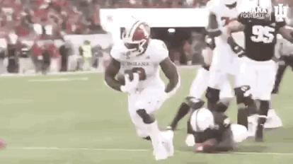 A Football Player Is Running With The Ball On A Field While A Player Is Laying On The Ground . GIF