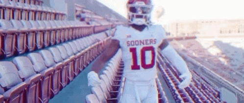 A Football Player Is Standing In A Stadium With Empty Seats . GIF