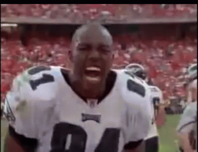 A Football Player Is Standing On A Field With His Mouth Open And A Crowd Behind Him . GIF