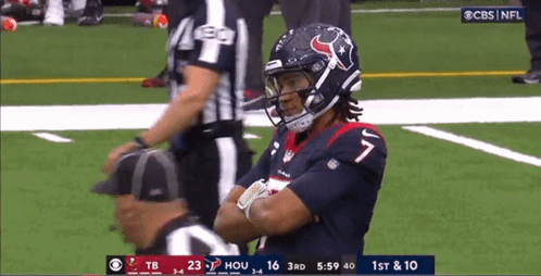 A Football Player Is Standing On The Field With His Arms Crossed And A Referee Standing Behind Him . GIF