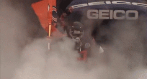 a football player is walking through a cloud of smoke while wearing a helmet .