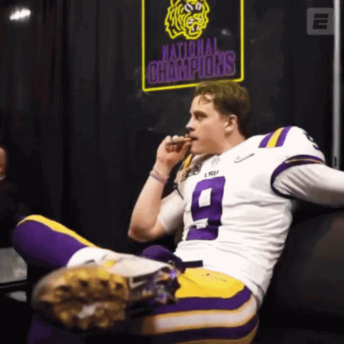 A Football Player Sitting On A Couch With A National Champions Sign Behind Him GIF