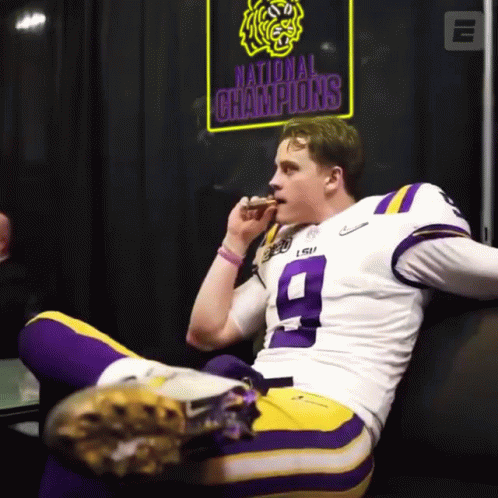 A Football Player Sitting On A Couch With A Sign That Says National Champions Behind Him GIF