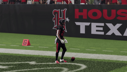 A Football Player Stands On The Field In Front Of A Sign That Says Texas GIF
