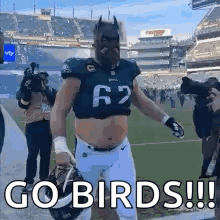 A Football Player Wearing A Batman Mask And A Helmet Is Walking On A Field . GIF