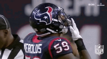 A Football Player Wearing A Helmet And Gloves Is Talking On A Cell Phone . GIF