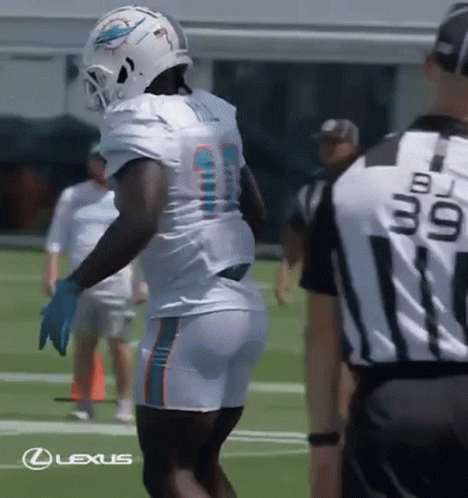 A Football Player Wearing A Helmet And Shorts Is Standing On A Field With A Referee . GIF