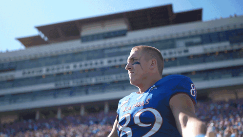 A Football Player Wearing A Kansas Jersey Stands In Front Of A Stadium GIF