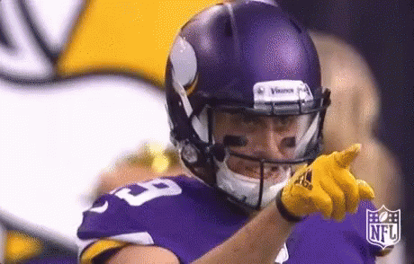 a football player wearing a purple helmet and yellow gloves is pointing .