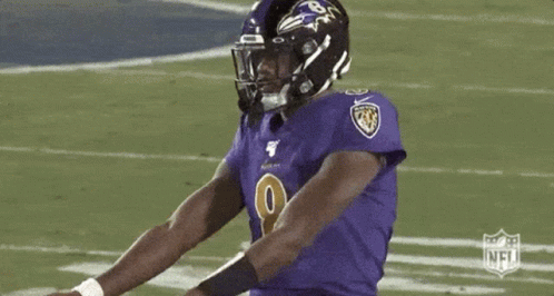 A Football Player Wearing A Purple Jersey And A Black Helmet Is Standing On A Field . GIF