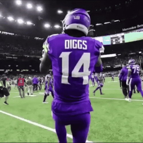 A Football Player Wearing A Purple Jersey With The Number 14 On It Stands On A Field . GIF