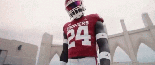 A Football Player Wearing A Red Jersey And A Helmet Is Standing In Front Of A Stadium . GIF