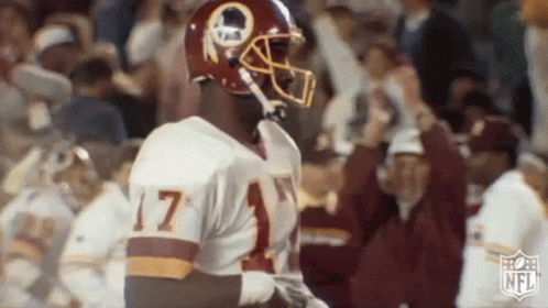 A Football Player Wearing A Redskins Uniform And Helmet Is Standing In Front Of A Crowd . GIF
