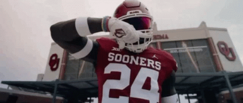 A Football Player Wearing A Sooners Jersey Is Standing In Front Of A Stadium . GIF