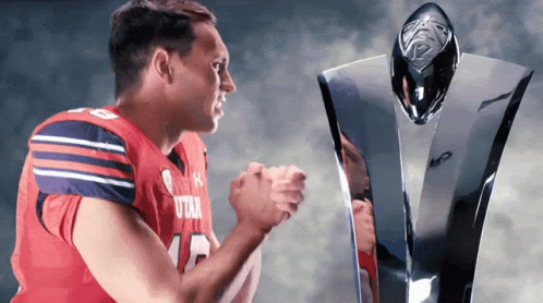 A Football Player Wearing A Utah Jersey Stands Next To A Trophy GIF