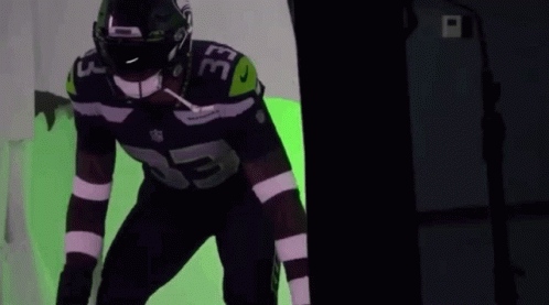 A Football Player With The Number 33 On His Jersey Is Standing In Front Of A Green Background . GIF