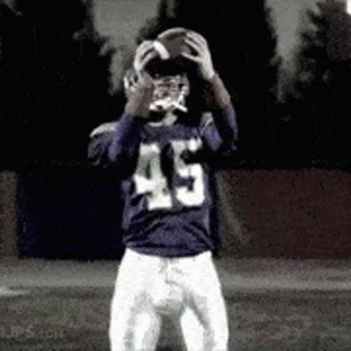 A Football Player With The Number 45 On His Jersey Is Holding A Football In His Hands . GIF