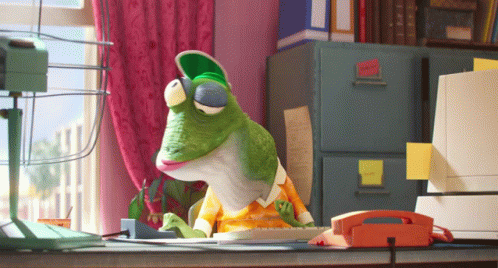 A Frog Is Sitting At A Desk With A Phone And A Fan GIF
