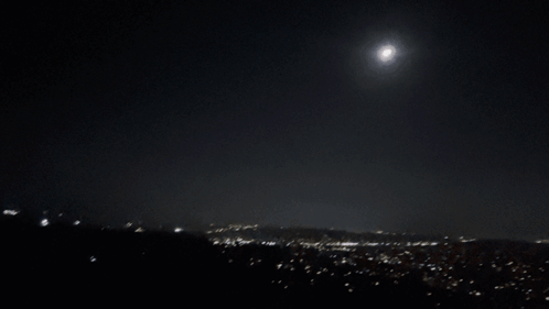 A Full Moon Shines Brightly In The Night Sky Over A City GIF