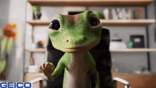A Geico Lizard Is Sitting In A Chair And Waving At The Camera GIF