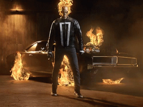 A Ghost Rider Is Standing In Front Of A Car That Is On Fire GIF