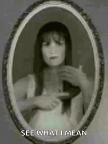 A Ghostly Woman Is Pointing At Herself In A Mirror . GIF