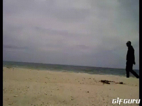 A Gif Of A Man Standing On A Sandy Beach With The Words Gif Guru Below Him GIF