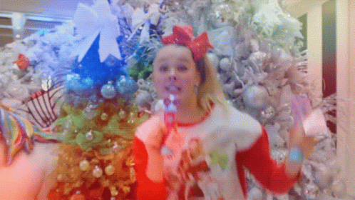 A Girl Blowing Bubbles In Front Of Christmas Trees GIF