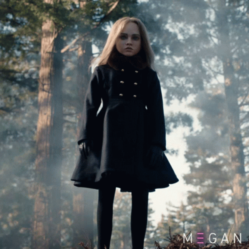A Girl In A Black Coat Stands In A Forest With The Name Megan On The Bottom Left GIF