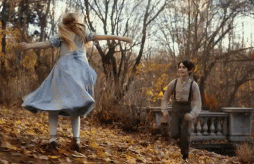 A Girl In A Blue Dress And A Boy In Suspenders Are Running Through A Forest . GIF