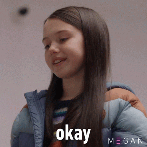 A Girl In A Blue Jacket Says Okay In Front Of A Megan Logo GIF