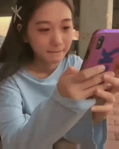 a girl in a blue shirt is holding a cell phone in her hands .