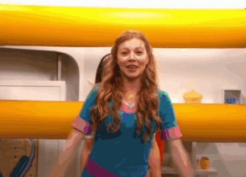 A Girl In A Blue Shirt Is Standing In Front Of A Yellow Wall With The Number 122 On It GIF