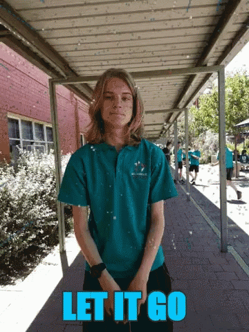 A Girl In A Blue Shirt Stands Under A Covered Walkway With The Words Let It Go GIF