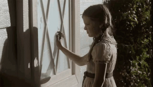A Girl In A Dress Is Standing In Front Of A Window With A Shadow On It GIF